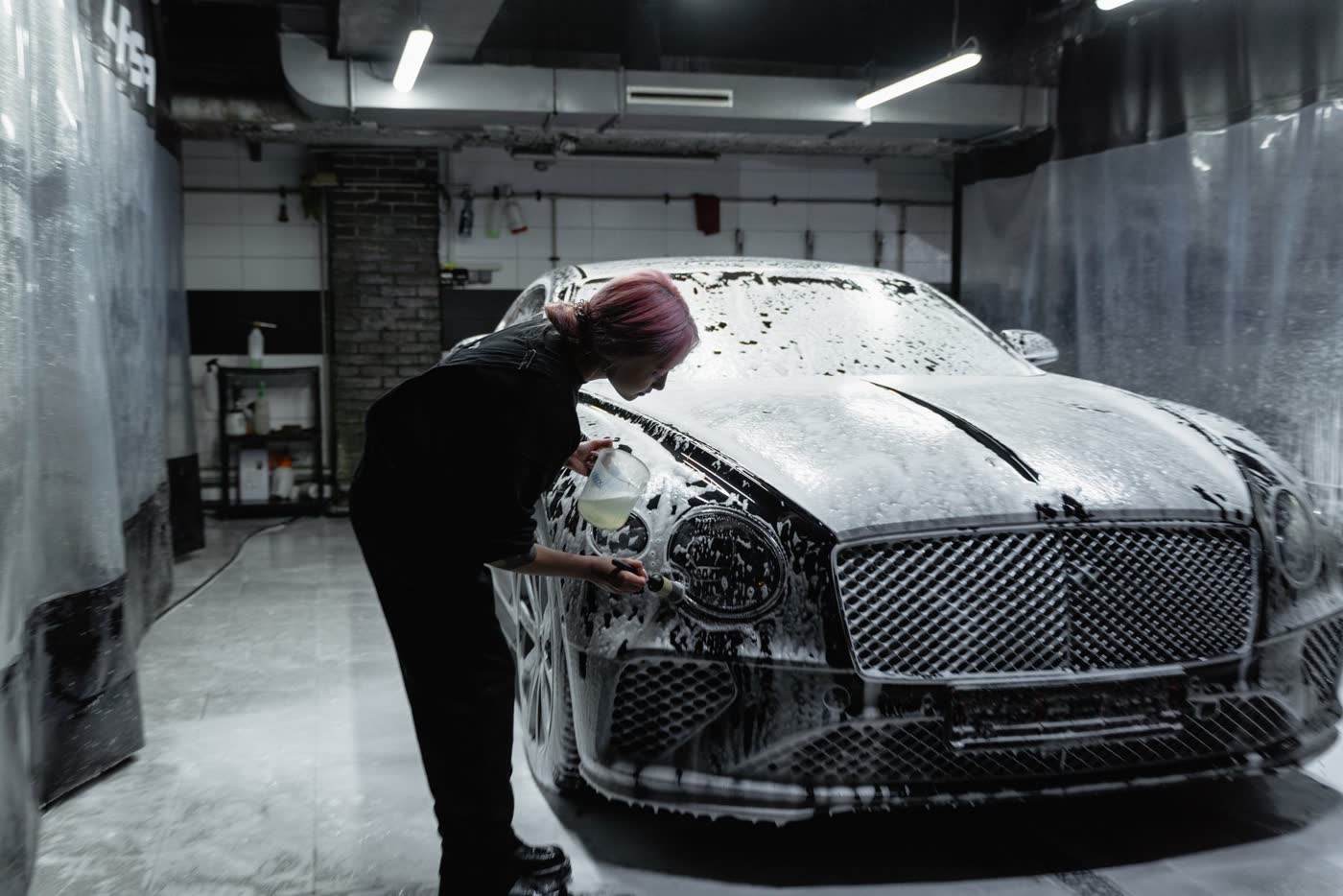 Detailer foam washing a luxury coupe inside a dark studio